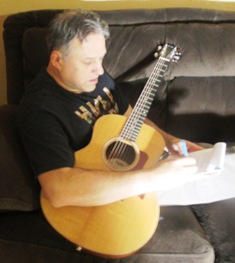 Free Original Songs - Dennis Hartman with guitar holding pen and paper and writing a song